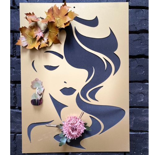 Pannello artistico oro con silhouette di profilo femminile intagliata, decorata con fiori artigianali e foglie autunnali su sfondo di mattoni neri.