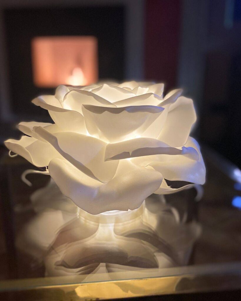 Ingresso notturno di una villa storica con scale in pietra decorate da rose giganti luminose e grandi rose bianche artigianali che incorniciano il portone scuro.