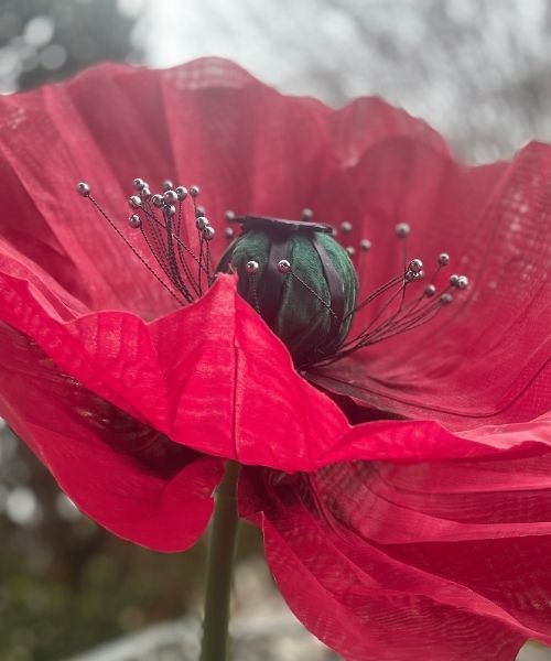 Papavero gigante rosso realizzato artigianalmente con petali traslucidi e dettagli decorativi, esempio di fiore scenografico per installazioni artistiche.