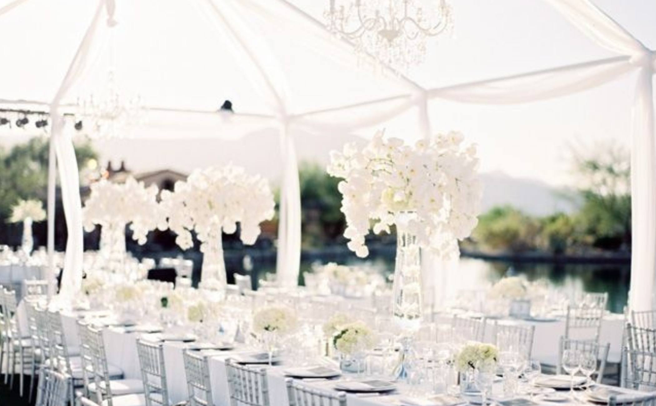 Allestimento matrimonio total white con tavoli eleganti, centrotavola alti di orchidee bianche e struttura in tessuto bianco vista lago.